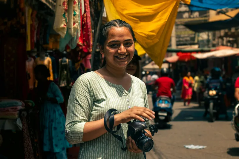 A smiling woman with a camera in a busy market street