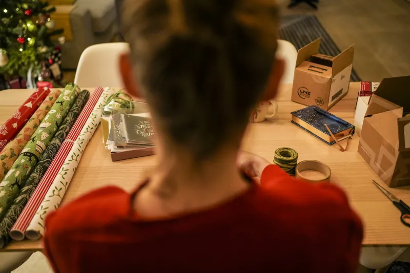 A seller wrapping gifts at a table covered in paper and ribbons