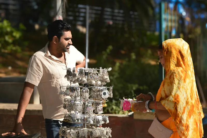 A jewellery seller showing silver pieces to a customer at his stall