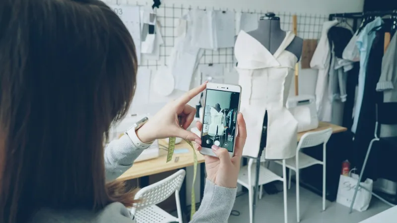 A designer photographing a dress on a mannequin with her phone