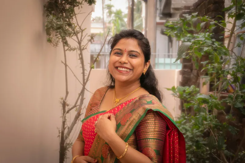 A smiling woman in a silk saree standing among plants