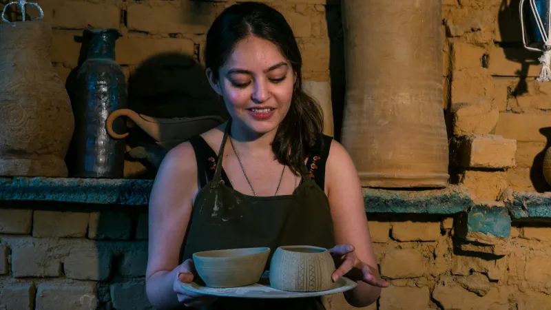 A smiling potter holding a tray of handmade clay bowls