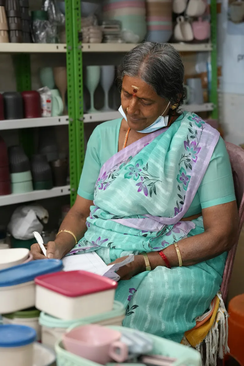 A shopkeeper in a saree writing a bill at her shop counter