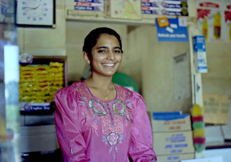A smiling shopkeeper in a pink kurta standing in her shop