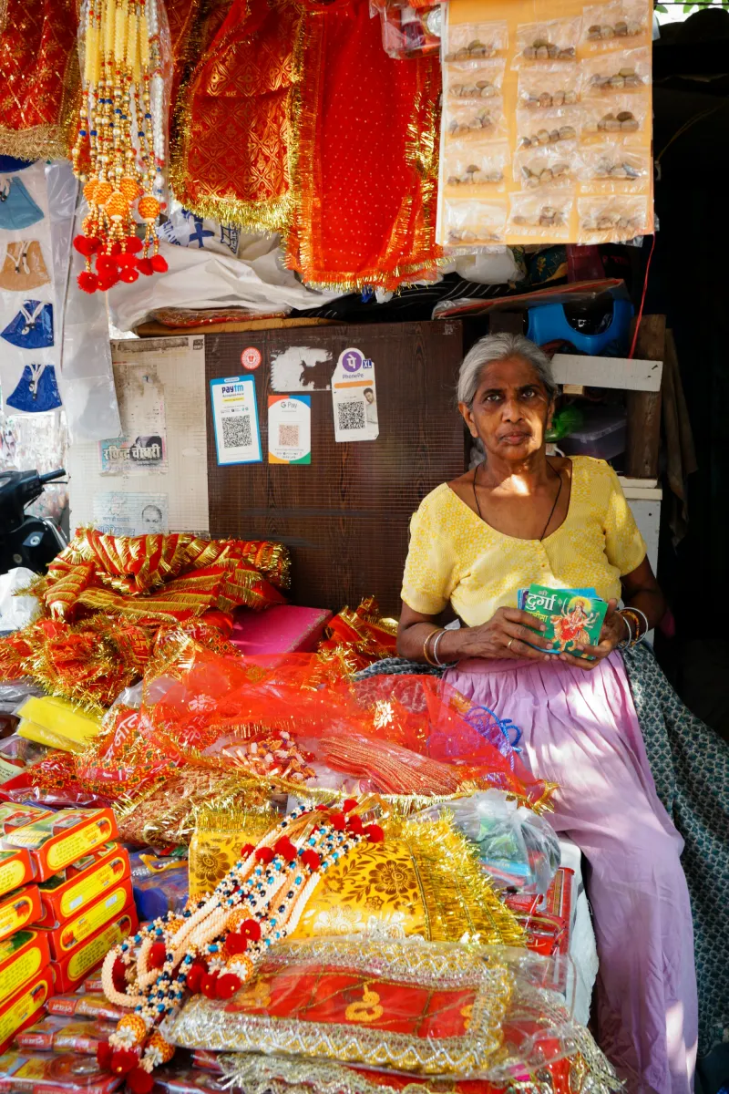 A shopkeeper at her stall of festive goods with payment QR codes on the wall behind her