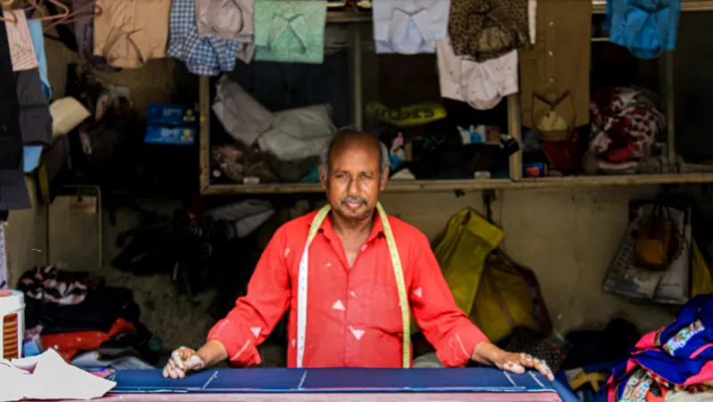 A tailor with a measuring tape smiling at his cutting table