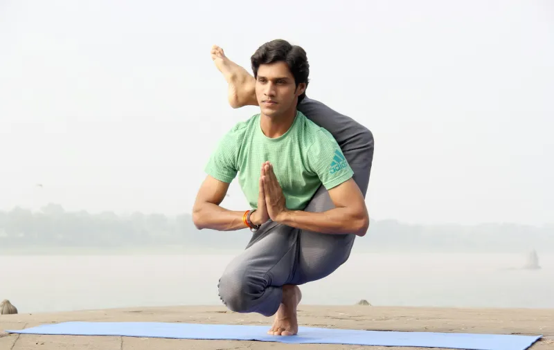 A yoga teacher balancing in a pose with hands joined, by a river at dawn